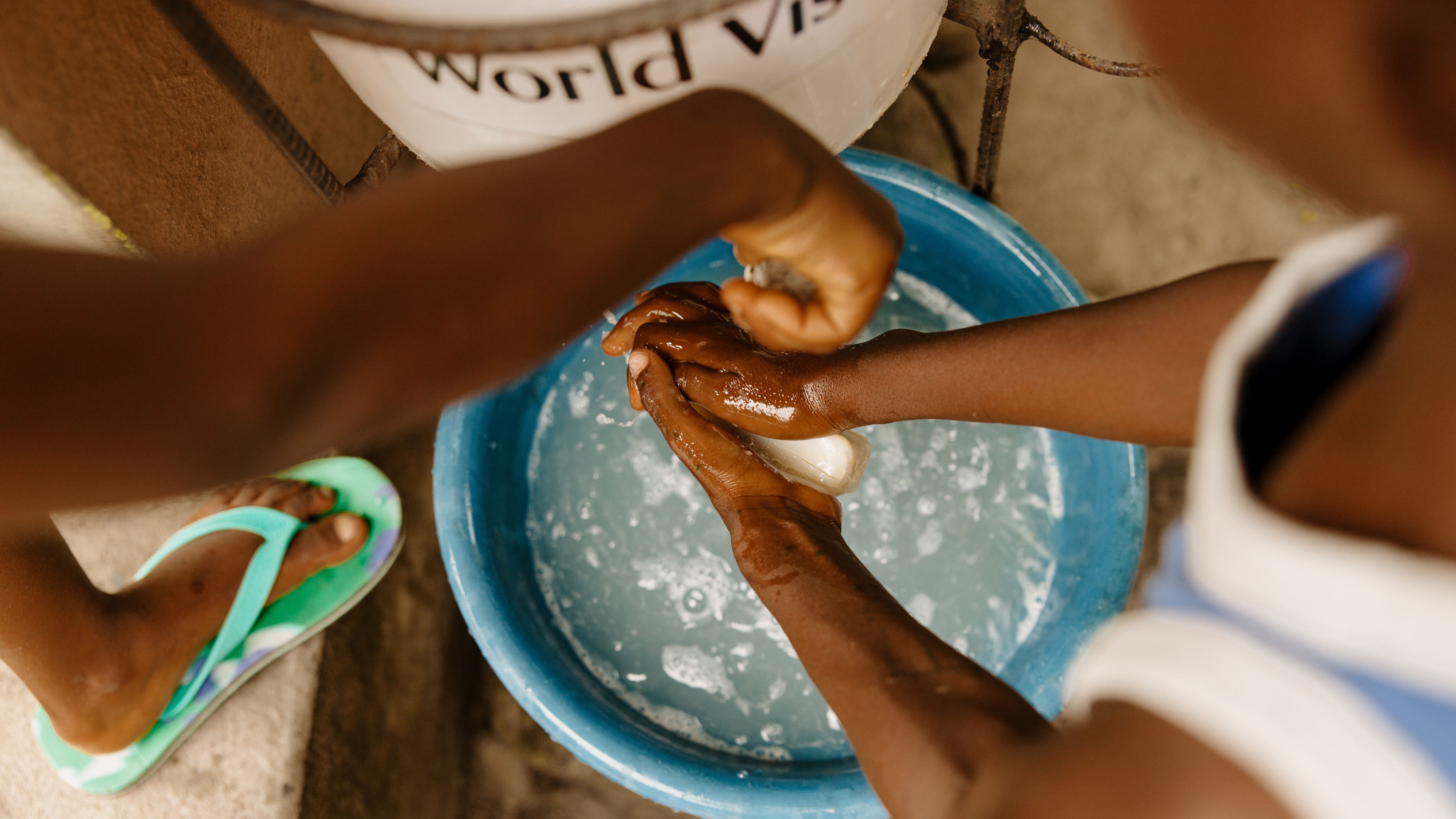 Close up shot of two children washing their hands with a bar of soap and tub of water