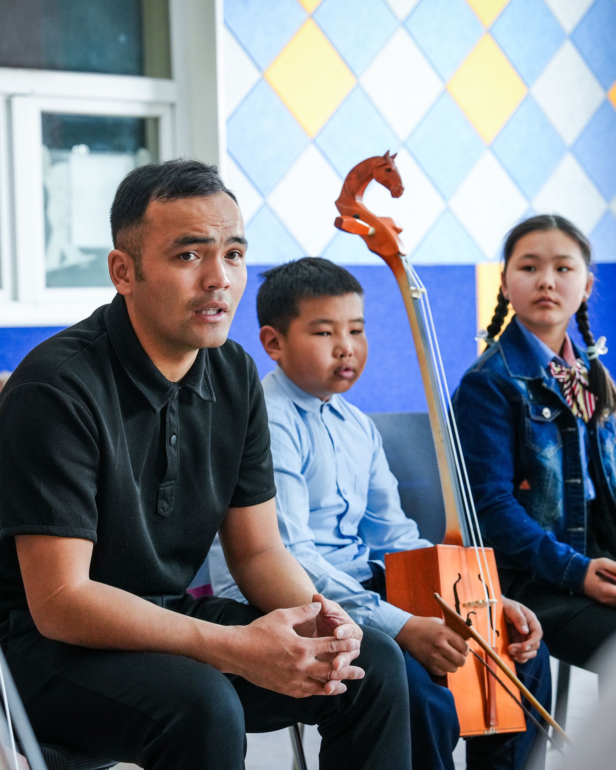 Bazar sits and talks to a group of students in a music class