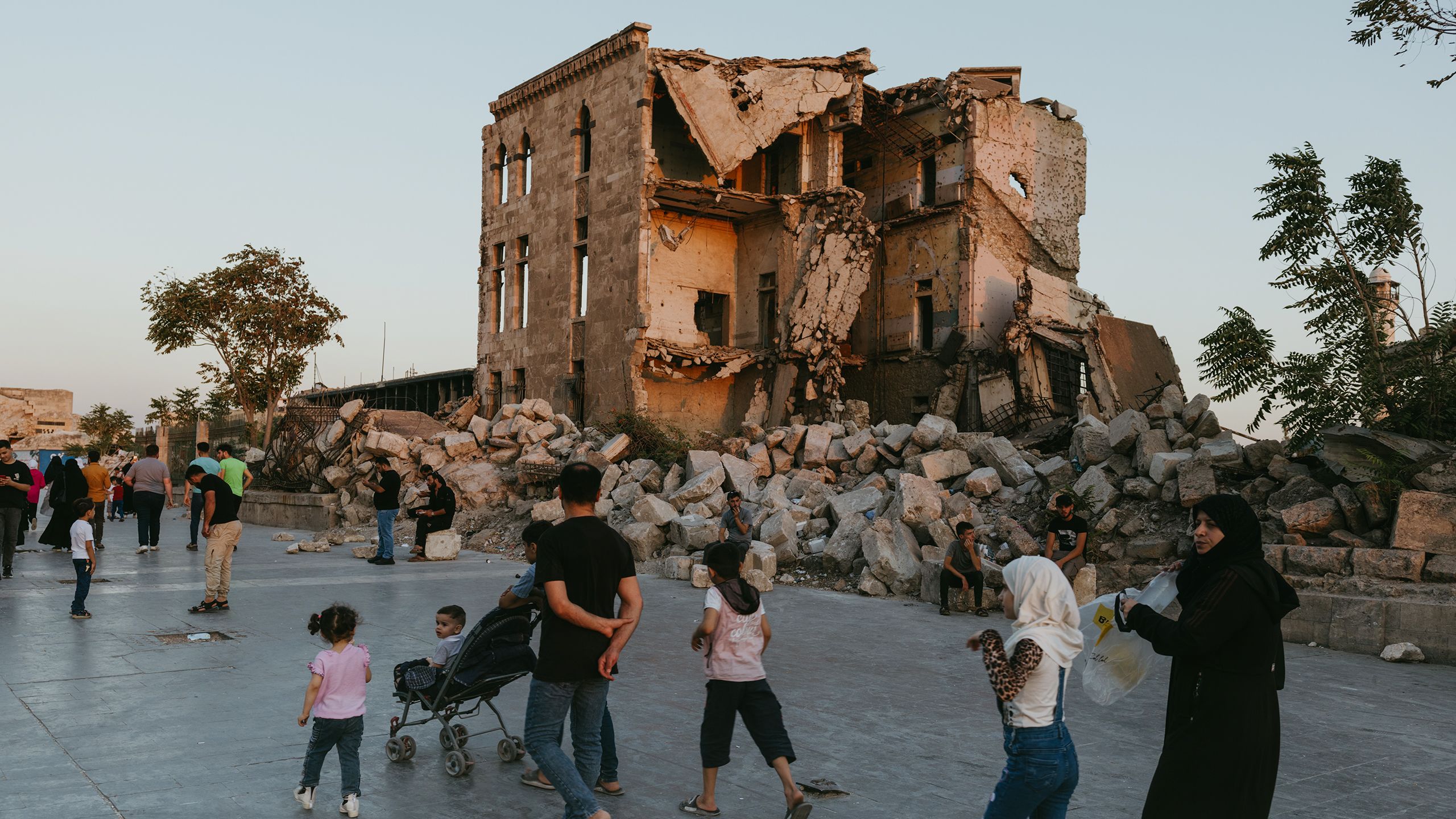 Families walk in front of damaged buildings in Syria due to conflict