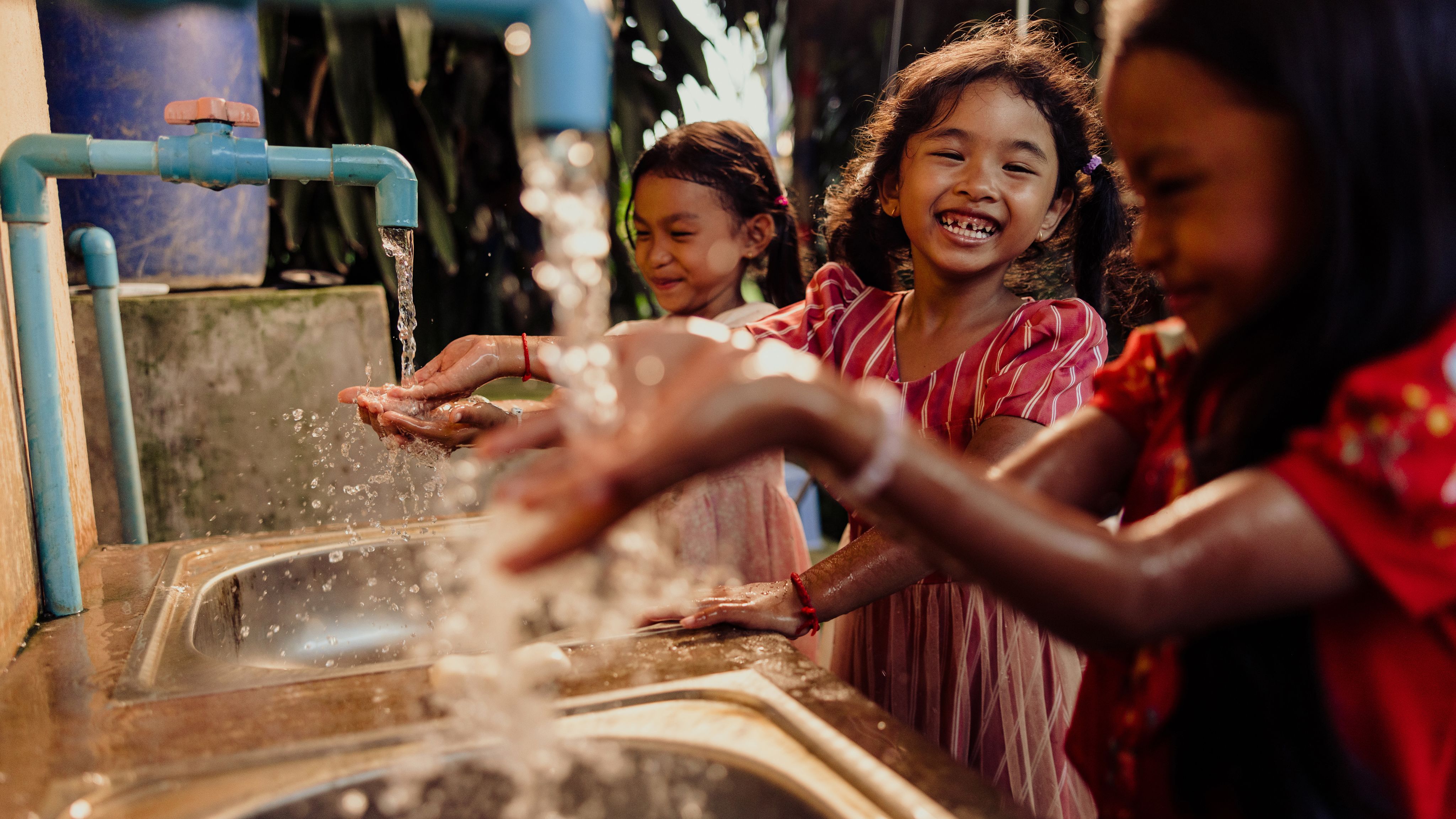 Three girls laugh together while washing their hands