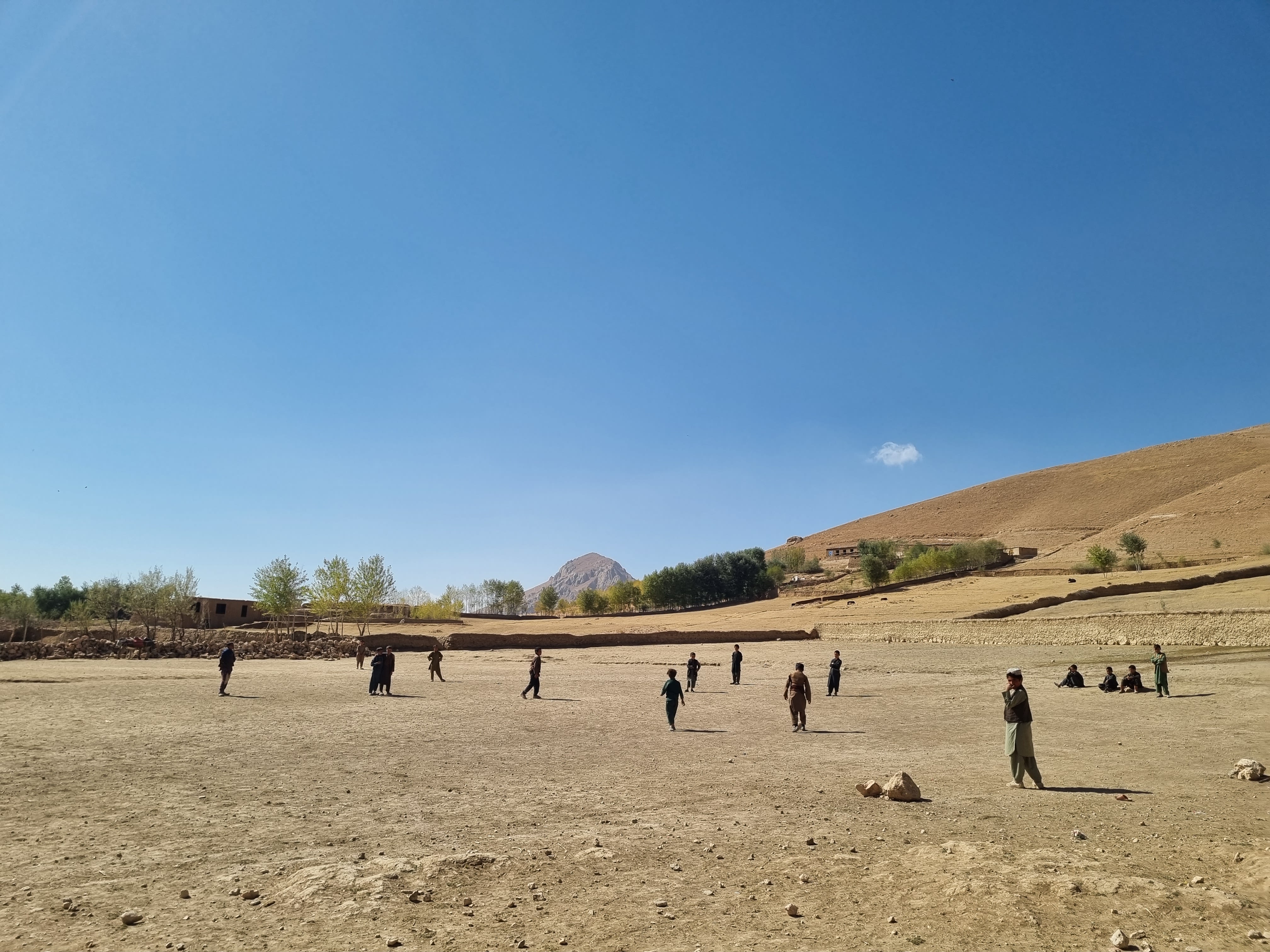 Children playing football in a dry landscape.
