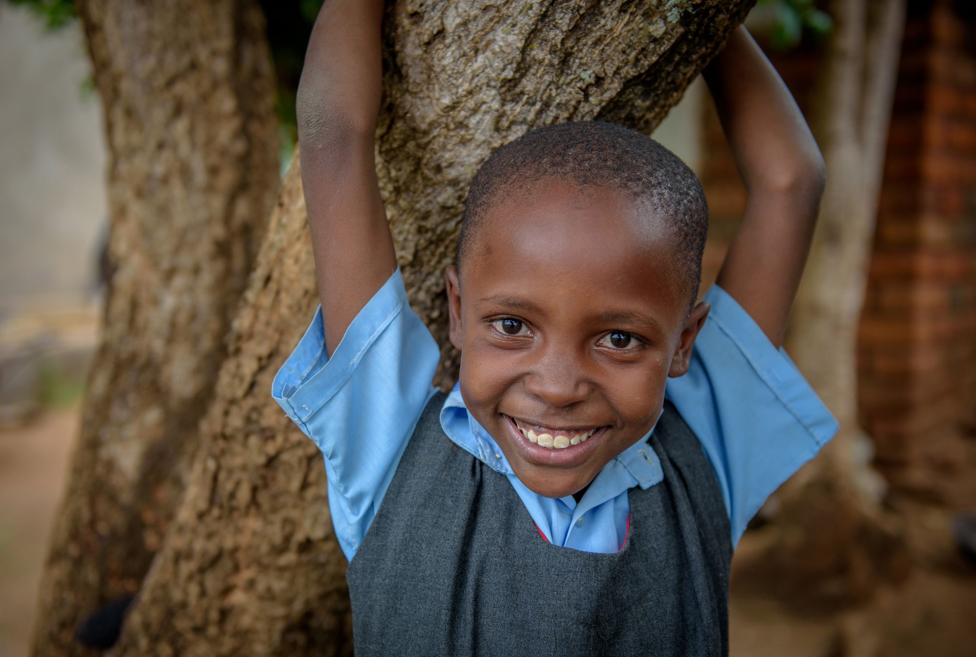 Sponsored child Mary holds on to a tree near her home.