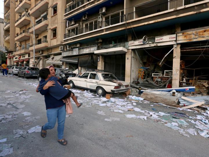 mother carries child through rubble along the streets of Beirut following deadly blast