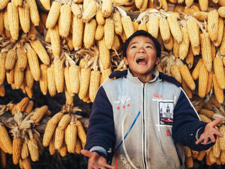 Child in China joyfully standing in front of backdrop of corn