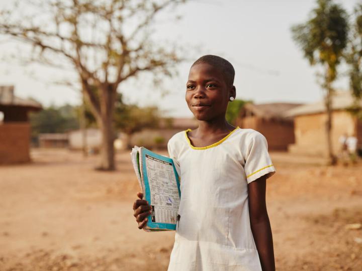 Child in Ghana stands with her school book in hand