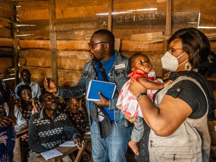 WVI staff speak to villagers inside of a hut