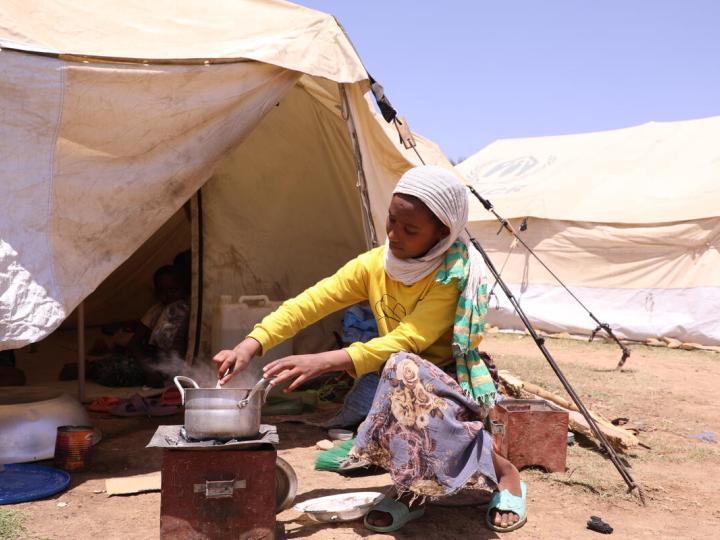 girl sits outside tent mixing food in a pot
