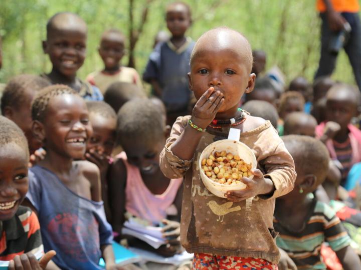 Child eats a bowl food of nuts while other children giggle in the background