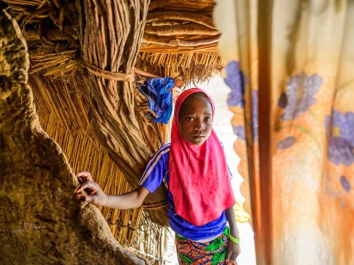 young girl stands inside the entrance to her family's hut