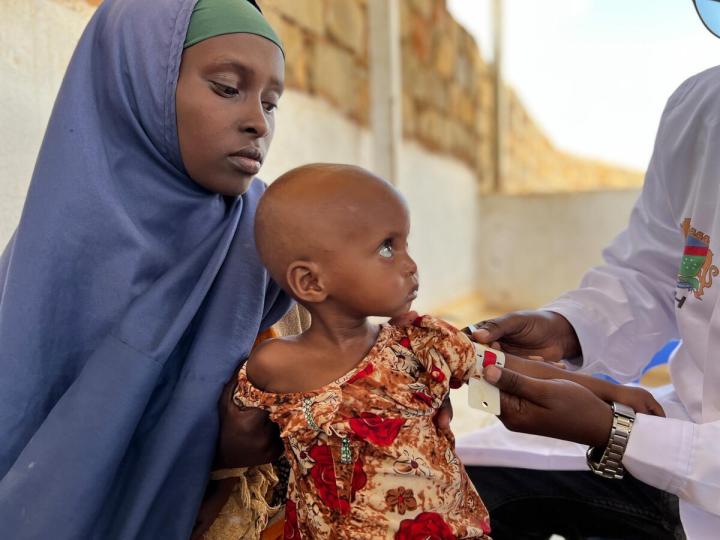 Mother holding her child as his mid upper arm circumference is tested for malnutrition