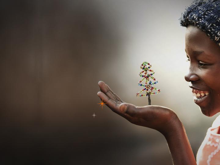 World Vision Child Sponsorship Christmas of Firsts Key Art _ Child looking at beaded Christmas tree in her hand