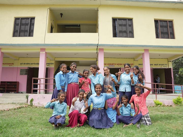 Girl students pose in front of their school.