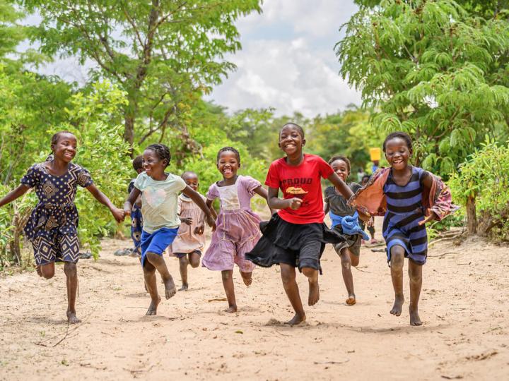 Girls hold hands and run down the road in Muchila AP, Zambia, where a World VIsion drilling crew is at work drilling a borehole to bring them clean water.