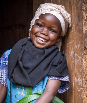 A girl stands against a wall smiling