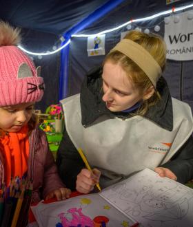 Nicolete Turcu, helps 4-year-old Arina with her coloring inside World Vision World Vision's child play area in Husi, Romania.