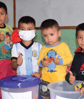 four boys sit in front of containers and show thumbs up for the camera 
