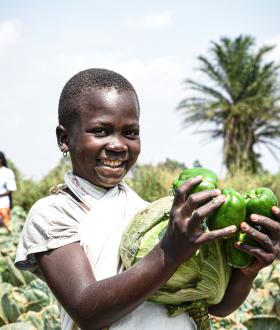 A girl holding cabbages and green pepper