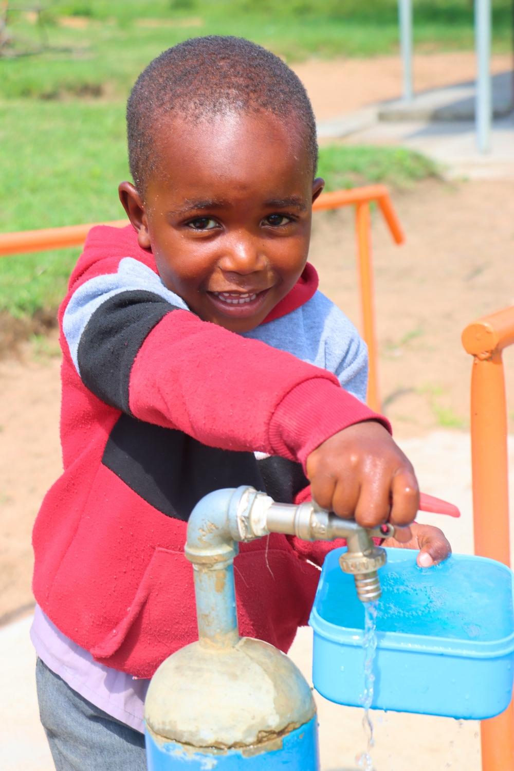 A Grade 1 learner fetching drinking water from one of the taps around his school.