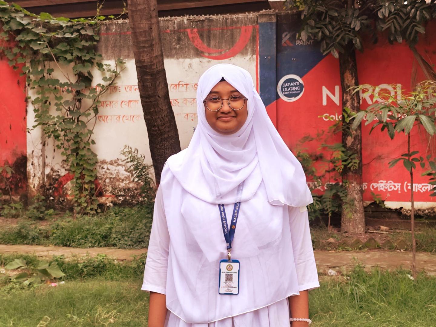 Tasnuva, a ninth-grade student in urban Dhaka standing Infront of her school