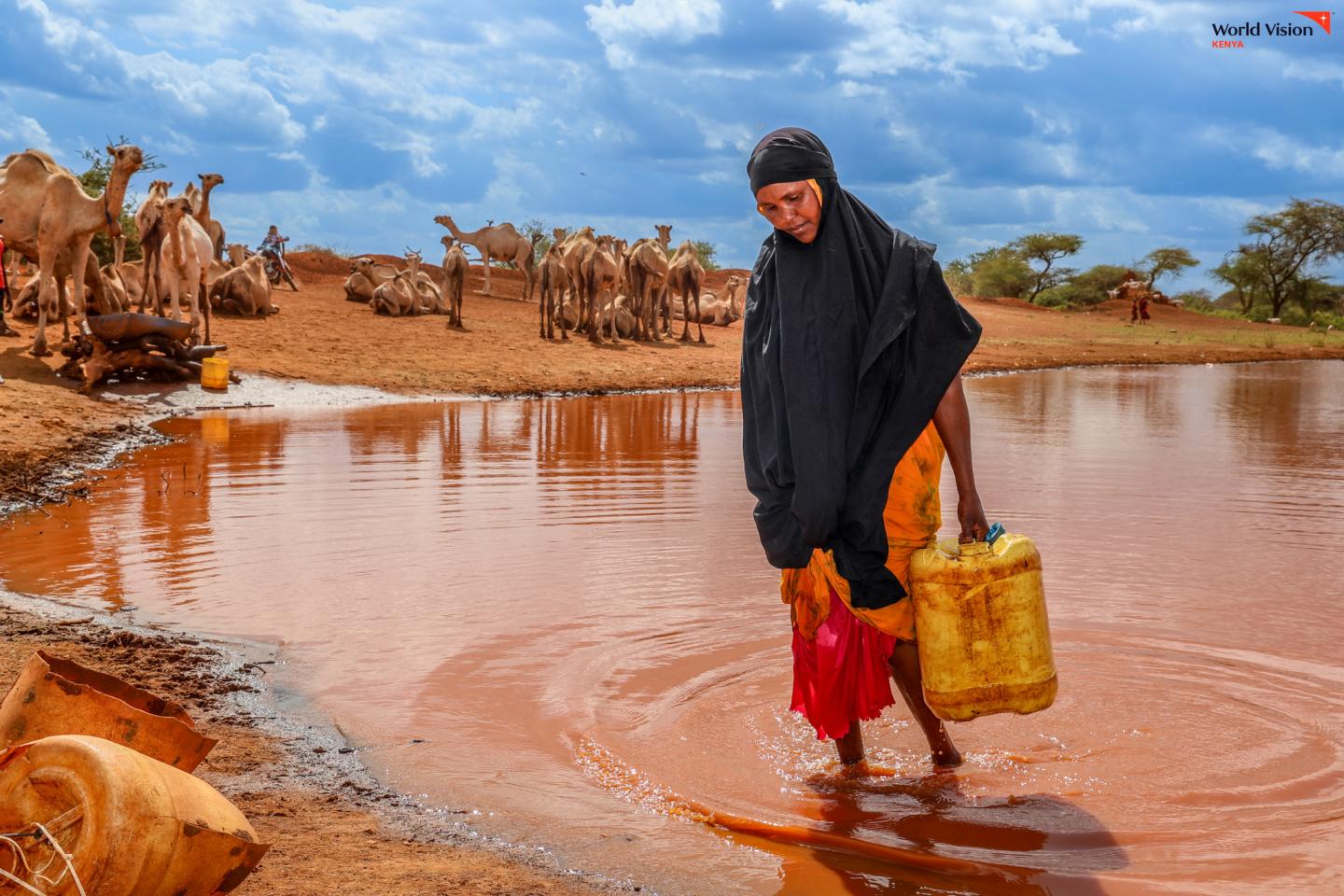 Habiba walks out of a water pan carrying a filled 20-litre jerrycan, ready to take the water home for her family's daily use. ©World Vision Photo/Mirriam Kioko