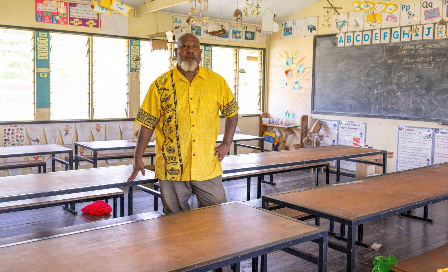 Teacher in Charge Mr. Noel Kwalimu posing with newly built student desks at Kupiano Elementary School
