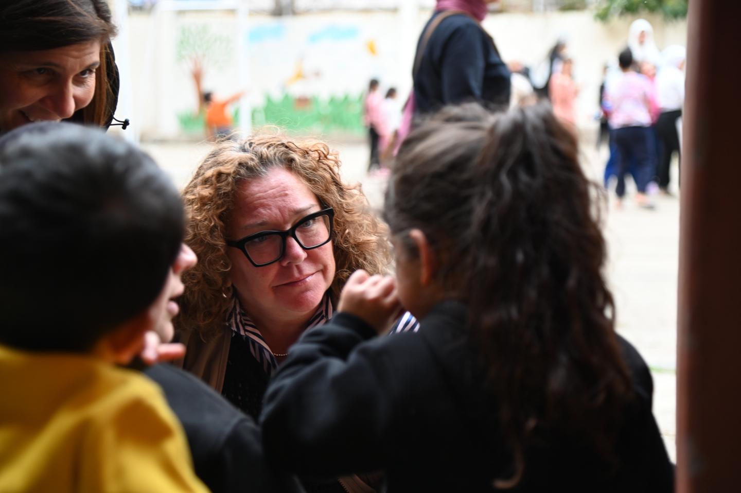 A woman with curly hair and glasses listens to two children