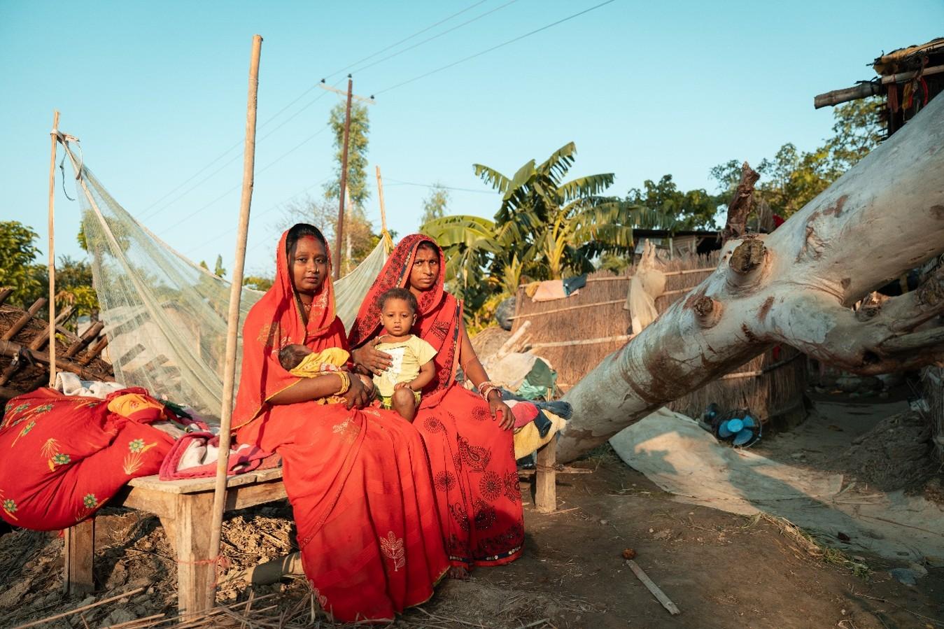 Sabita and her mother-in-law hold her children on their laps amid the wreckage caused by the flood.