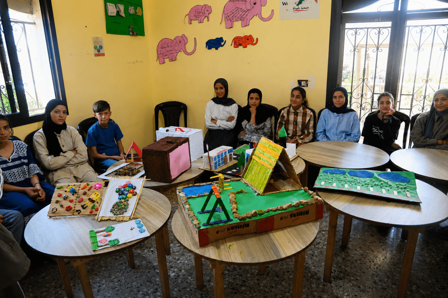 Children gather around tables displaying colourful handmade models and creative projects inside a learning centre in Wadi Khaled, Akkar.