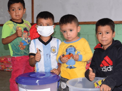 four boys sit in front of containers and show thumbs up for the camera 