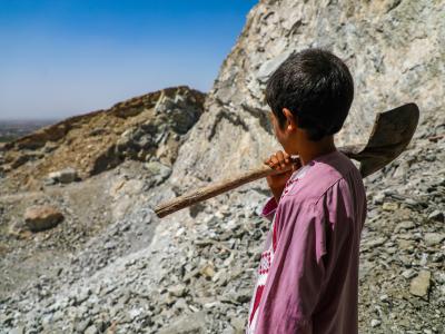 Mujeb*, a 12 year old in Afghanistan, poses with a shovel near the rocks he must break for work. 