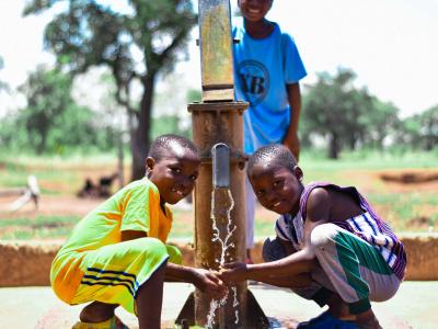 Two children drinking water from the tap. 