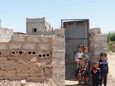 Khloud’s* children standing in front of their collapsing home in Syria