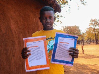 Sydney beams with joy as he holds a collection of letters sent by his sponsor, a reminder of their meaningful connection.