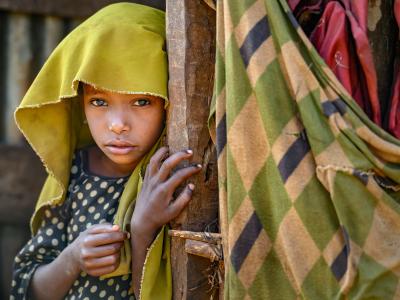 A young girl peeks shyly from behind a wooden post, eyes wide with wonder.