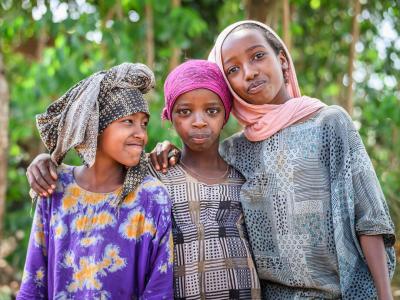 Three girls from Ethiopia smile at the camera with their arms around each other.
