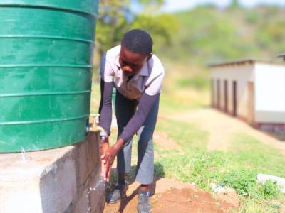 Mndeni washing hands from a water tap in his school. 