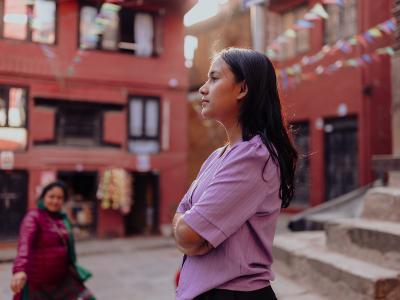 A young woman stands with arms cross looking into the distance in city streets