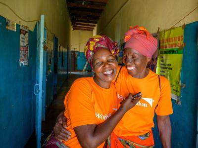 Two women wearing orange World Vision shirts smile at the camera