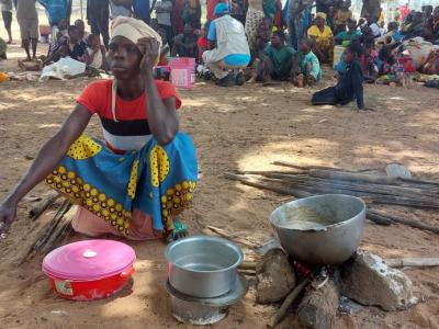 A woman sits close to a fireplace where meals are prepared.
