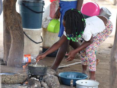 A child in an accommodation center is preparing a meal in a pot that is already half empty for a family with many members.