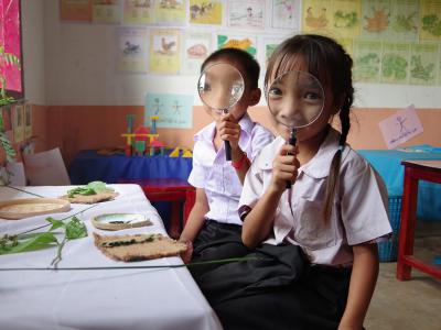 Two school children hold up magnifying glasses to their eyes.