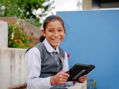 A student sits outdoors with a tablet in hand, taking part in a digital learning activity