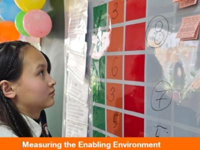A young girl looks at a whiteboard with various colored papers and notes taped on. The title of the report is in the middle of the image.