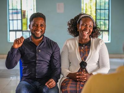 A man and woman sit next to each other, both smiling.