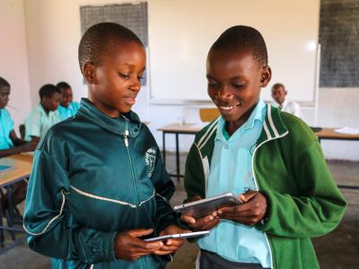 Two learners are showing each other something from the tablets.