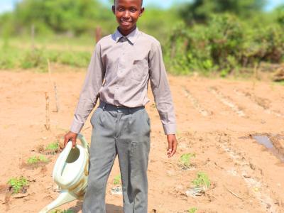 A learner standing inside a school garden after watering vegetables.