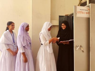 Female students line up at a World Vision hygiene corner in Dhaka school to receive sanitary pads from a teacher.