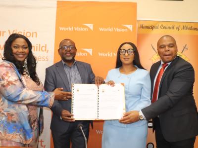 Four people posing for a camera holding a signed document. 