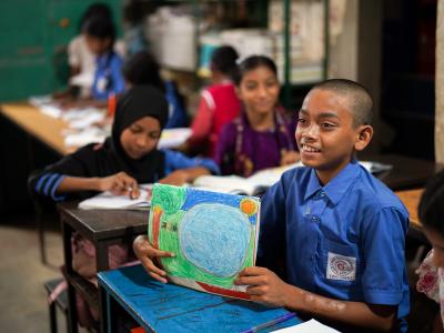 Wearing a crisp blue school uniform, Sipon sits at a desk in his Dhaka classroom, eager and ready to learn.
