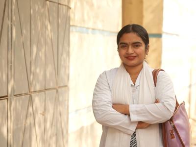 Bhavna stands outside a hospital in her white clinical uniform, smiling as she pursues a career in healthcare after overcoming child marriage.